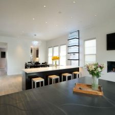 A well illuminated living room has the TV and a chimney on. Two stylish white speakers stand on each side of the TV.