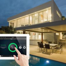 Close up of a Control4 tablet in someone's hands in their backyard by the pool. The tablet shows the home's security system.