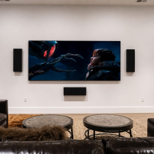 Custom home theater with a large wall-mounted display, front speakers, center speaker, subwoofer, and equipment rack