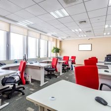 Open-plan office with white desks, computer monitors, and red chairs.