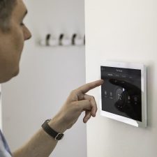Man adjusting a wall-mounted smart thermostat touchscreen.