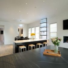 Open-plan modern living space with in-ceiling speakers, a wall-mounted TV, and a linear fireplace