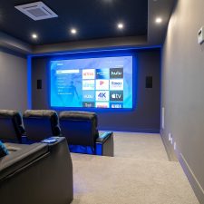 Dedicated home theater with tiered leather seating, a large screen, in-wall speakers, recessed lighting, and blue accent lighting