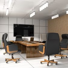 Modern conference room with wall-mounted display, wood table, and black office chairs.