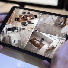 A shot of a person holding a tablet showing different monitored rooms within their home for home security purposes.